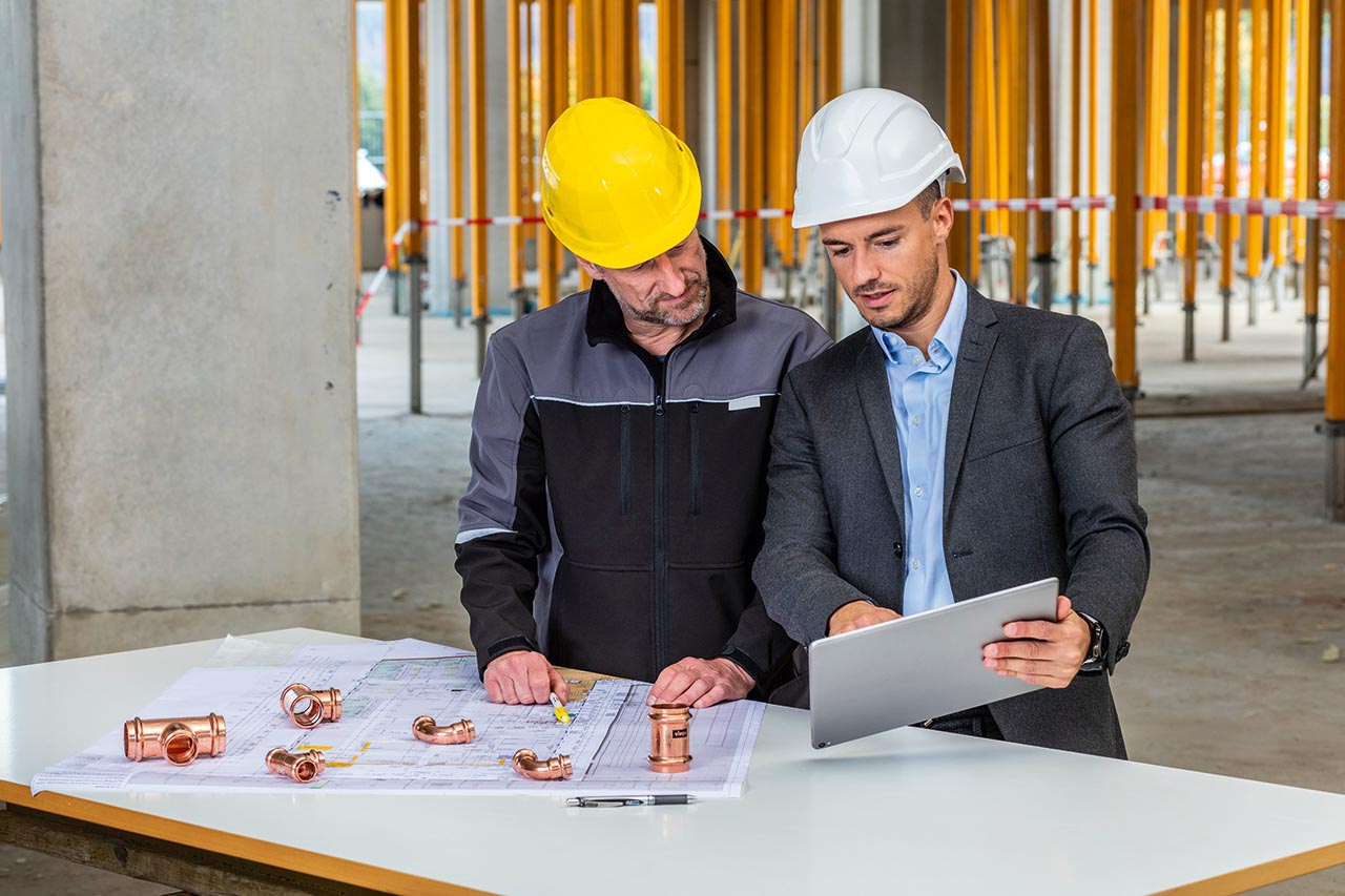 Building site environment, interior side view: Planning on site using the Viega Tool Services modules by craftsmen and planners using a tablet. Piping technology, system technology, new generation, press guns, Profipress, tools, tool management, web application, Viega Tool Services app, location, administration, ballpoint pens.